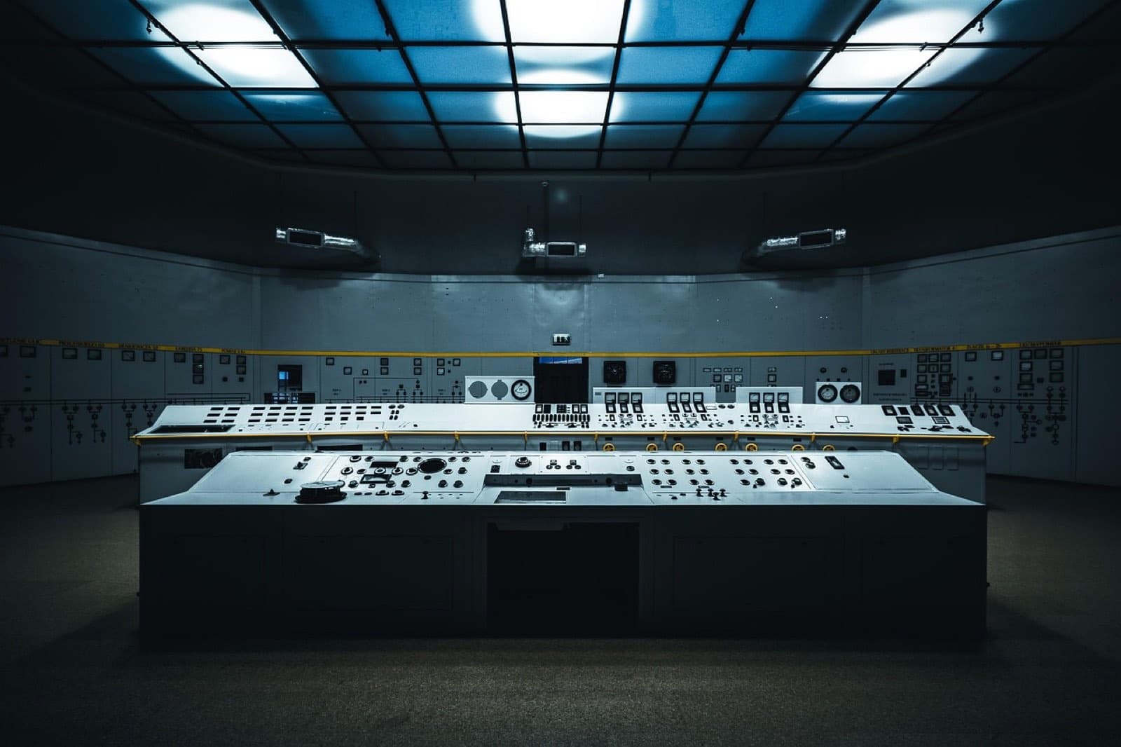 An industrial control room: one long instrument desk of switches and dials facing a wall of gauges, lit from above.