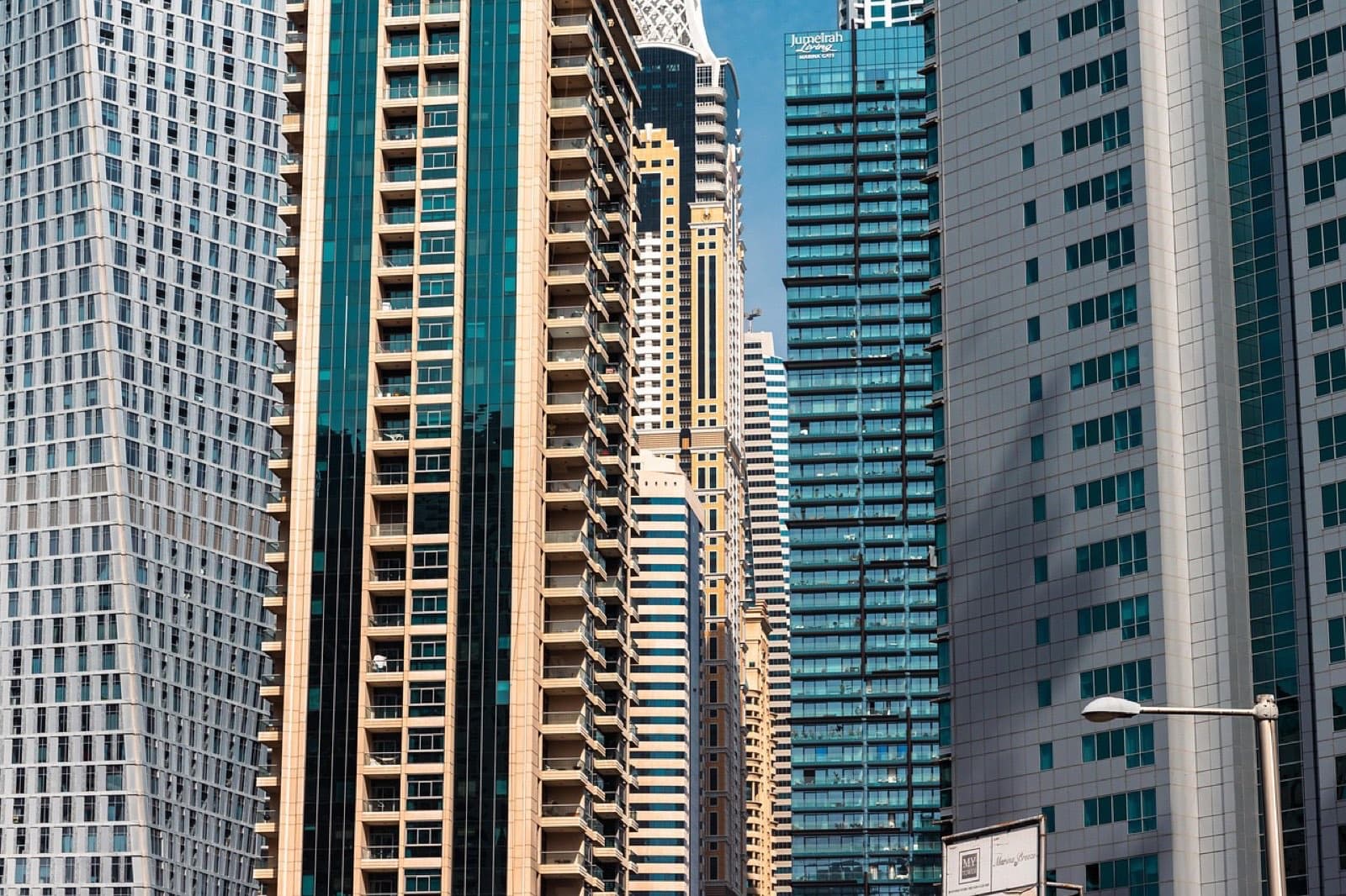 Towers packed close together in Dubai's business district, seen from street level in daylight.
