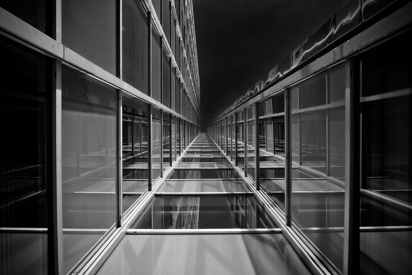 A glazed walkway photographed head-on in black and white, its frames repeating into the distance.