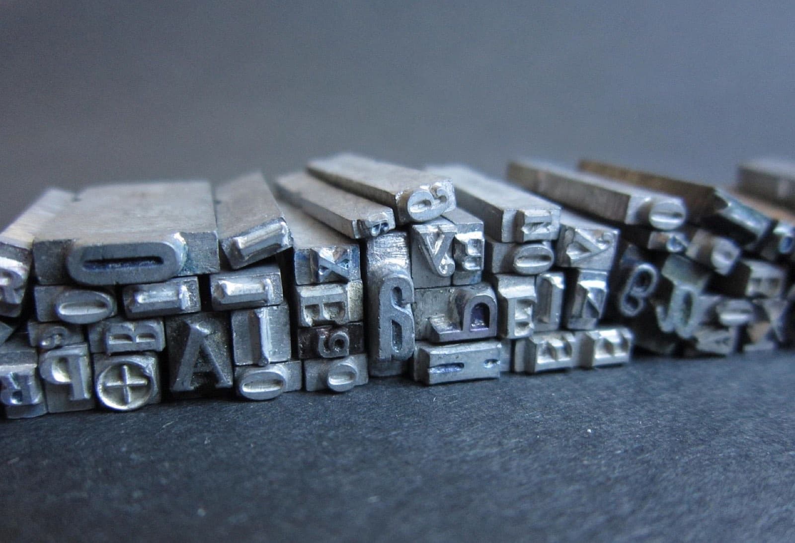 A row of metal letterpress type standing on a grey surface, letters facing the camera.